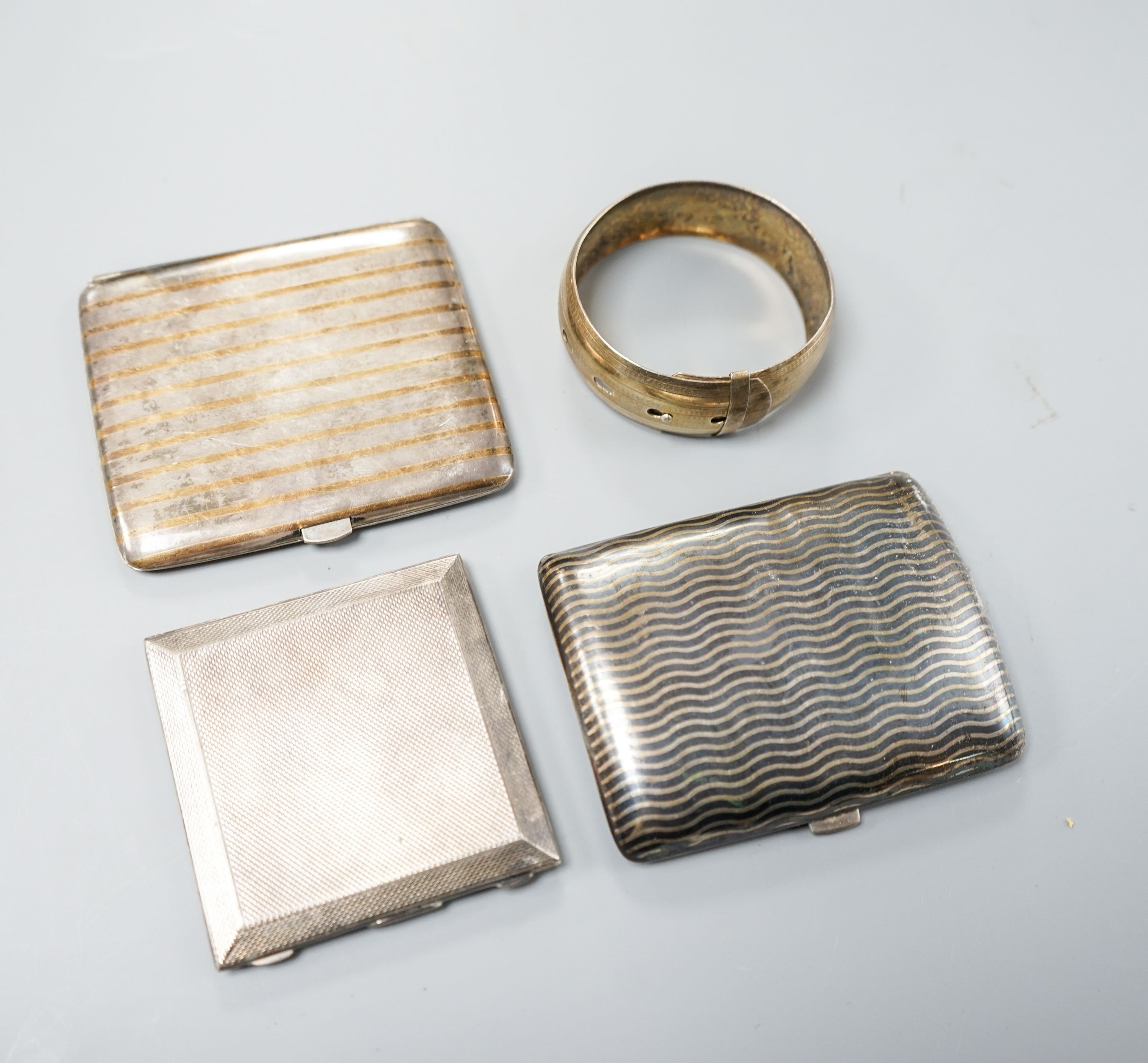 An 800 white metal and niello cigarette case,9cm, a Dutch gilt and white metal cigarette case, an engine-turned silver powder compact (a.f.) and a white metal bangle.